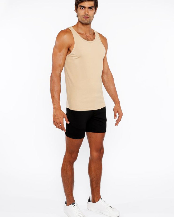 Man wearing a beige tank top and black shorts on a white background