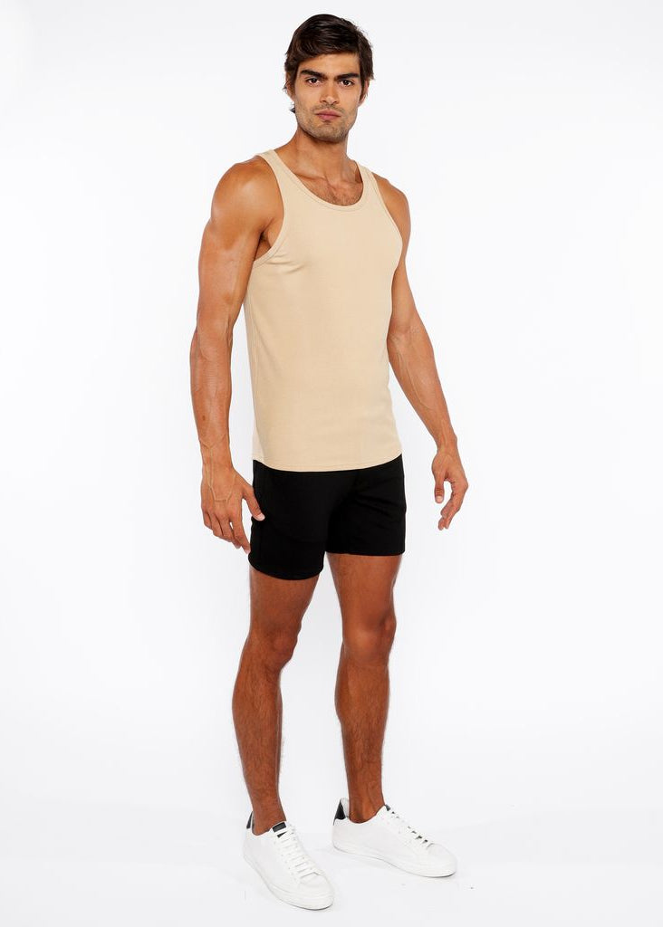 Man wearing a beige tank top and black shorts on a white background