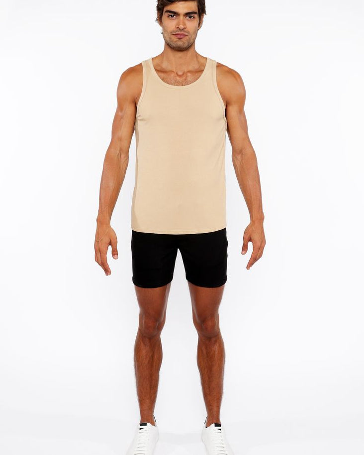 Man wearing a beige tank top and black shorts on a white background