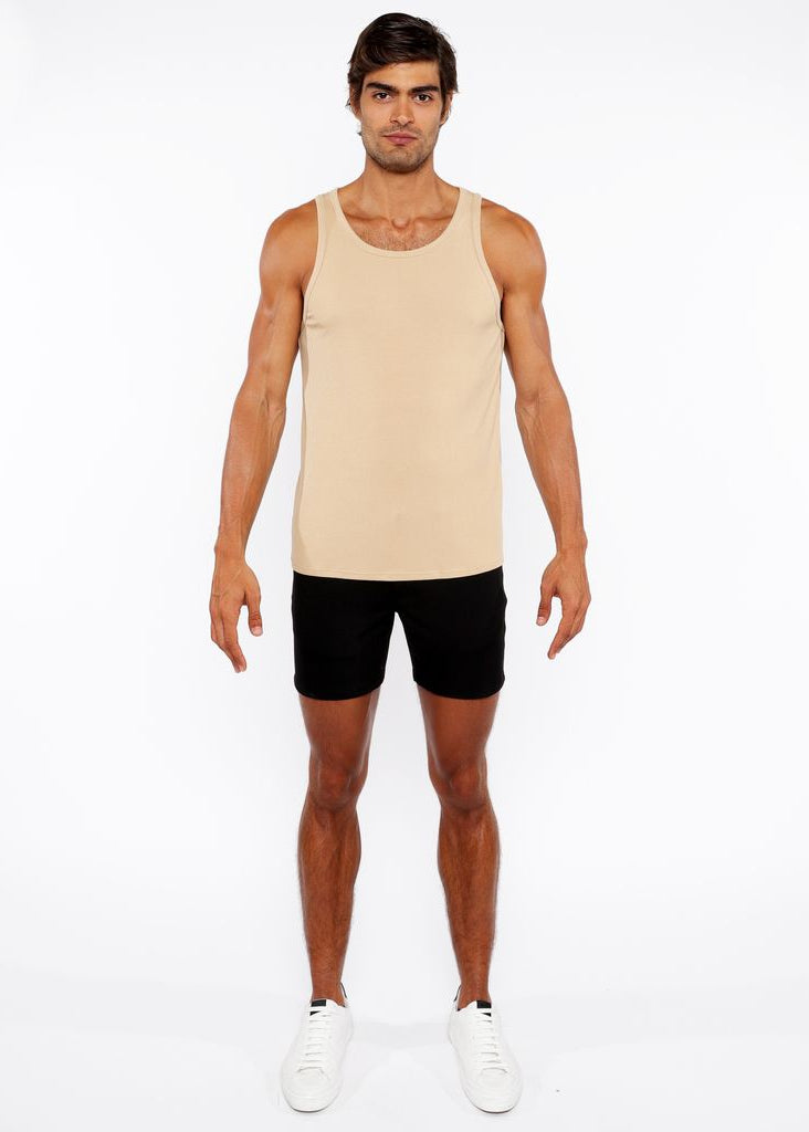 Man wearing a beige tank top and black shorts on a white background