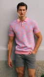 Man wearing a pink patterned polo shirt and gray shorts standing against a plain wall.
