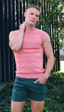 Man wearing a pink sleeveless shirt and green shorts standing outdoors.