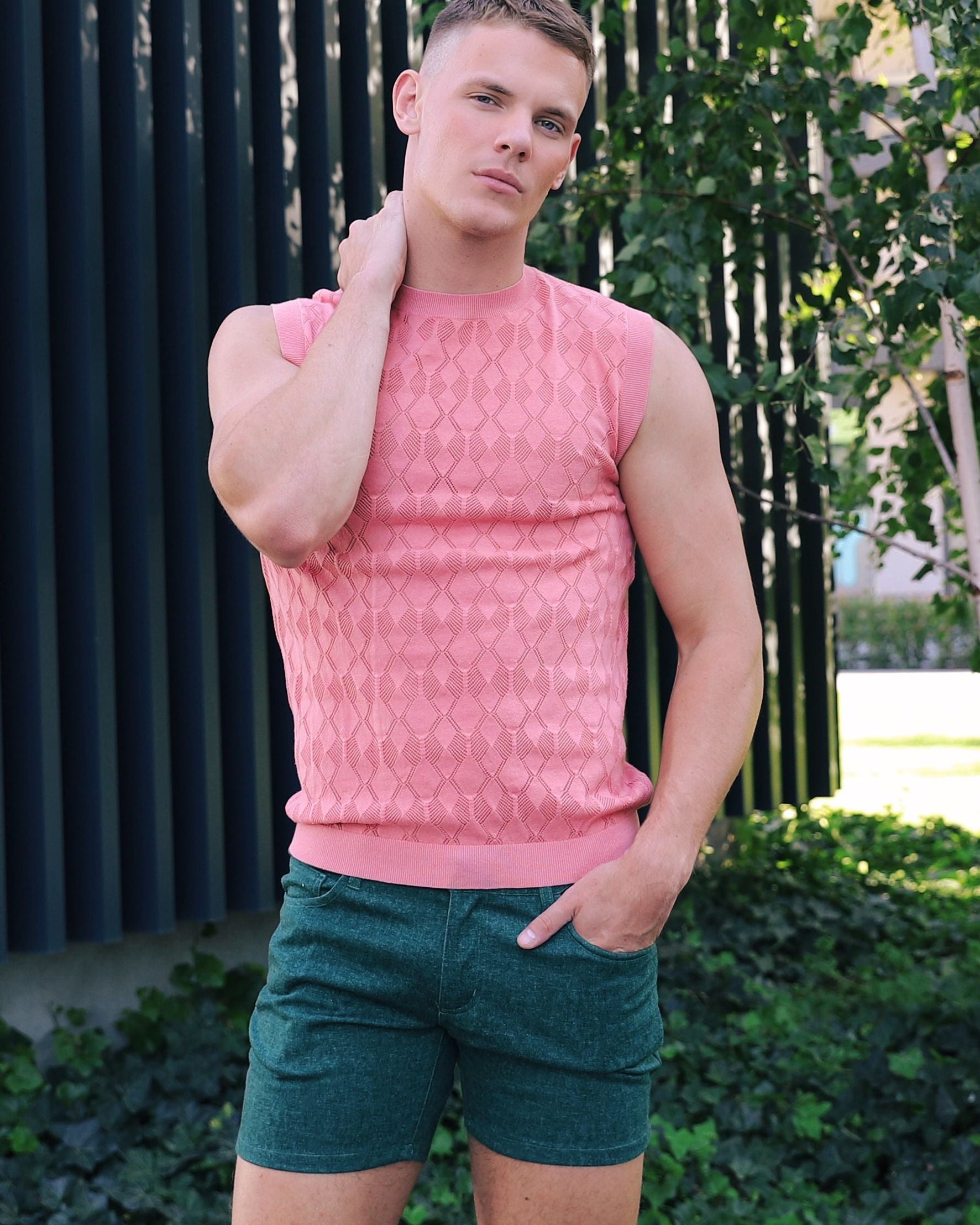 Man wearing a pink sleeveless shirt and green shorts standing outdoors.