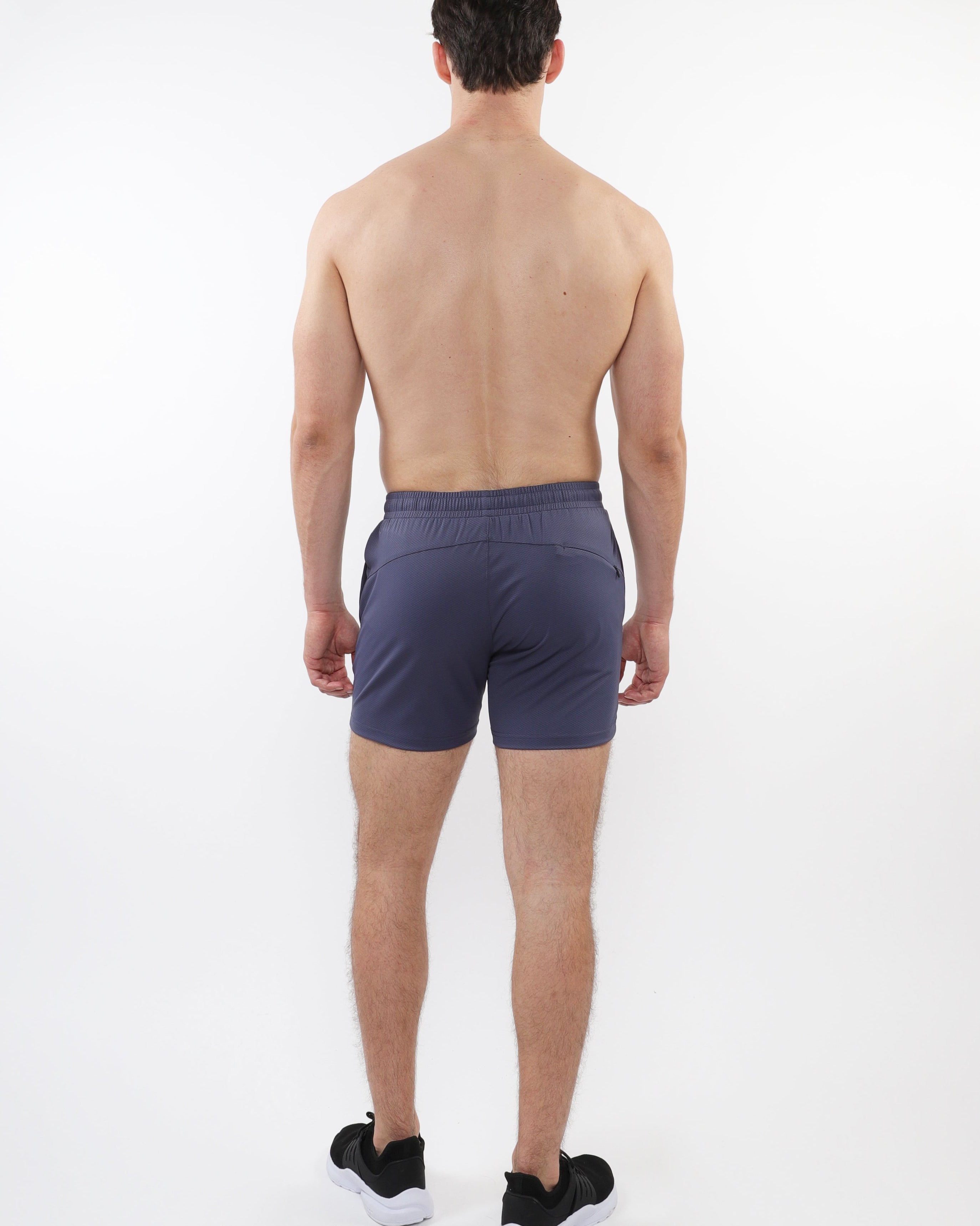 A male model facing away from the camera wearing slate gray mesh stretch performance shorts with a shorter inseam.