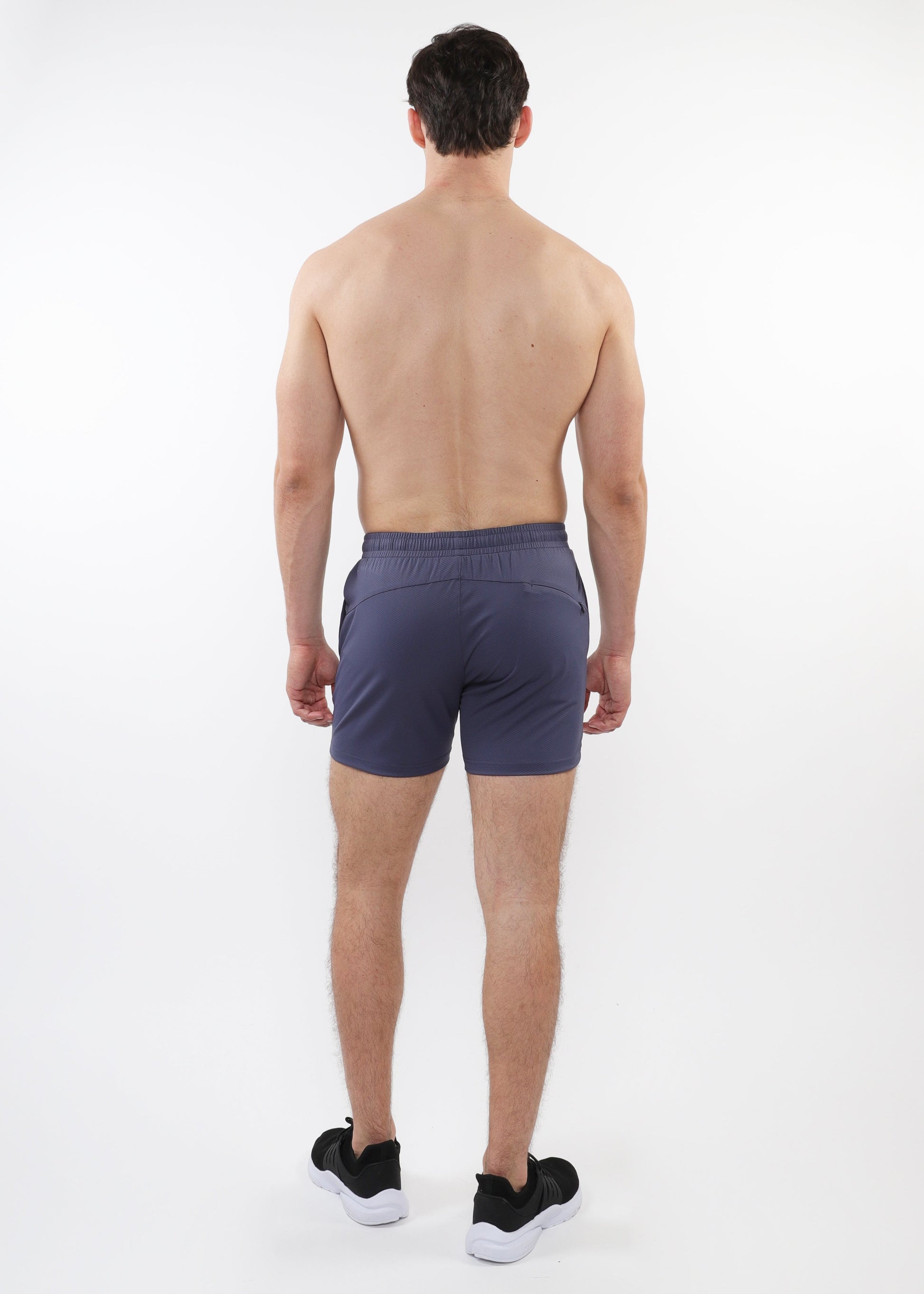 A male model facing away from the camera wearing slate gray mesh stretch performance shorts with a shorter inseam.