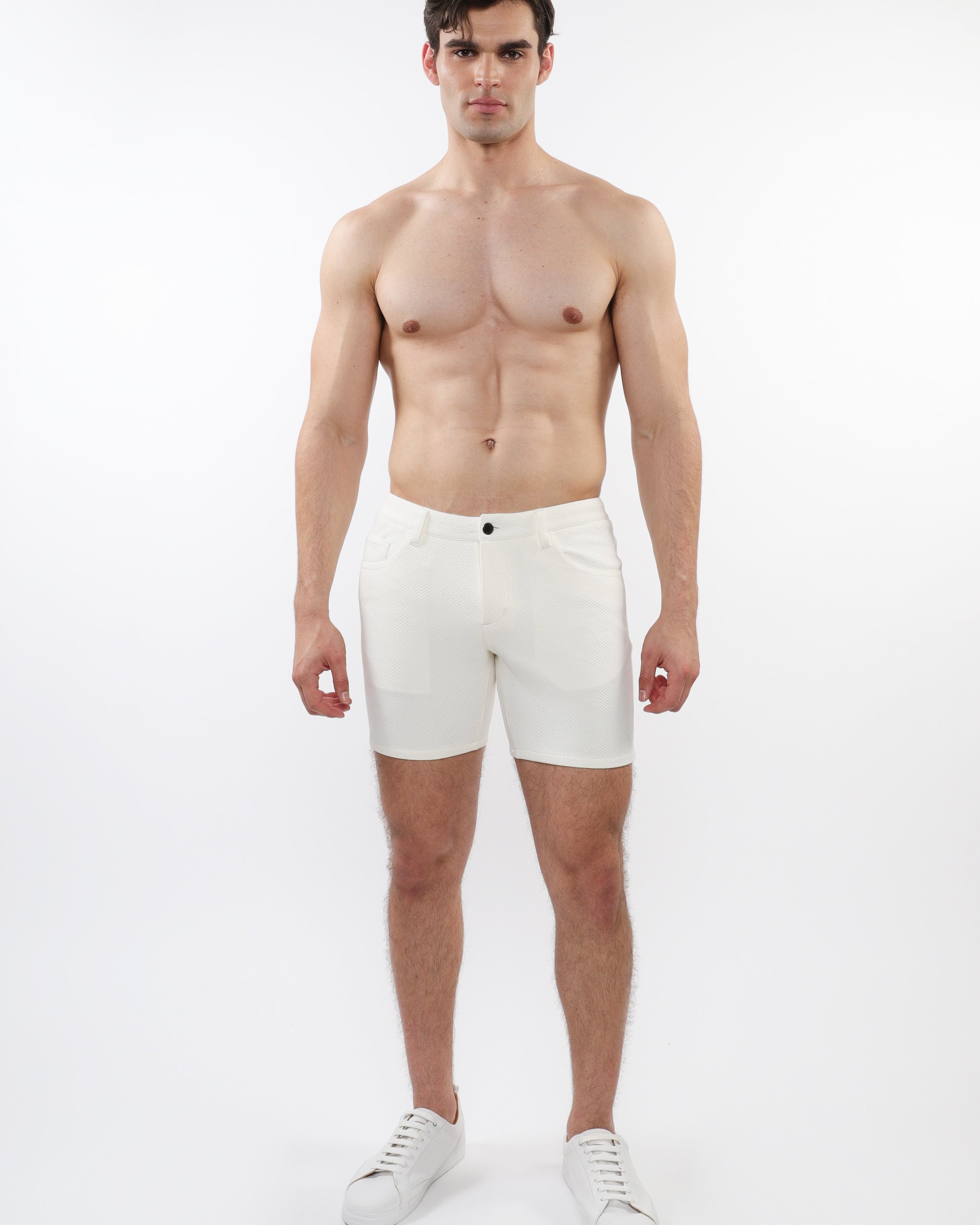 A model wearing white stretch knit shorts with a 5-inch inseam and a slim fit through the thighs and seat.