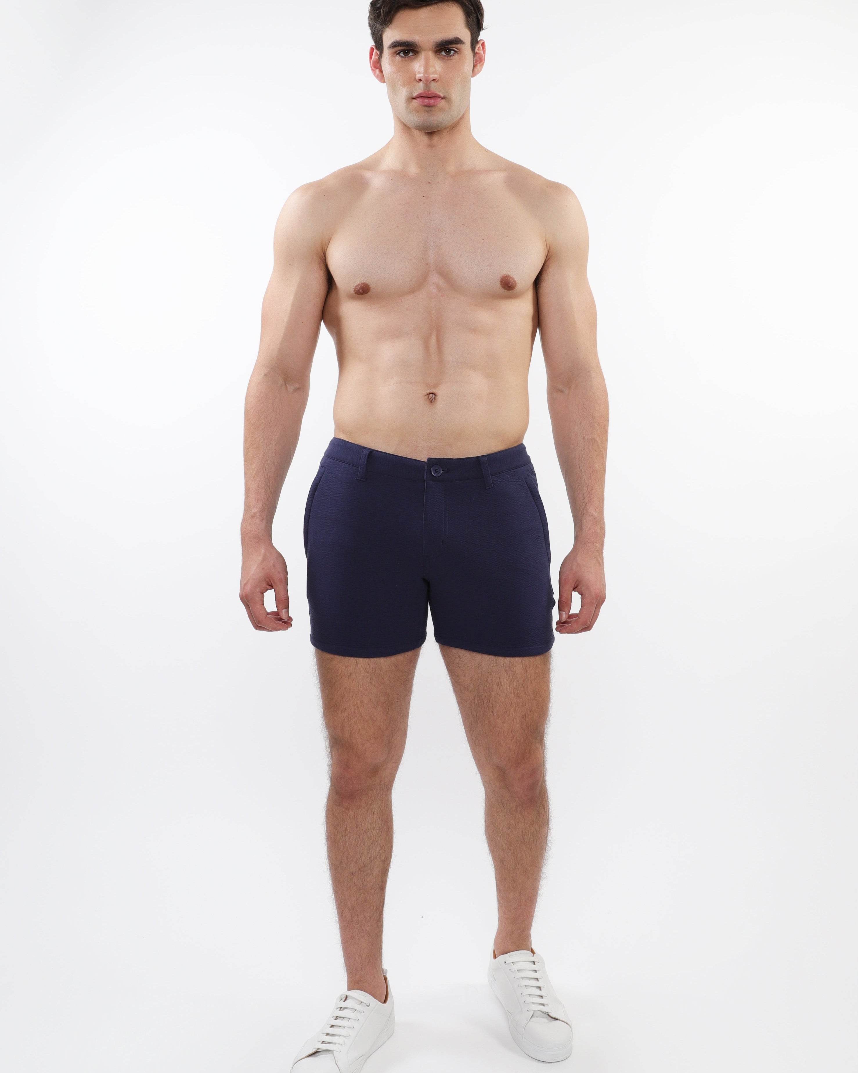 A model wearing navy blue chino shorts with a zipper fly and slim fit, standing against a white background.