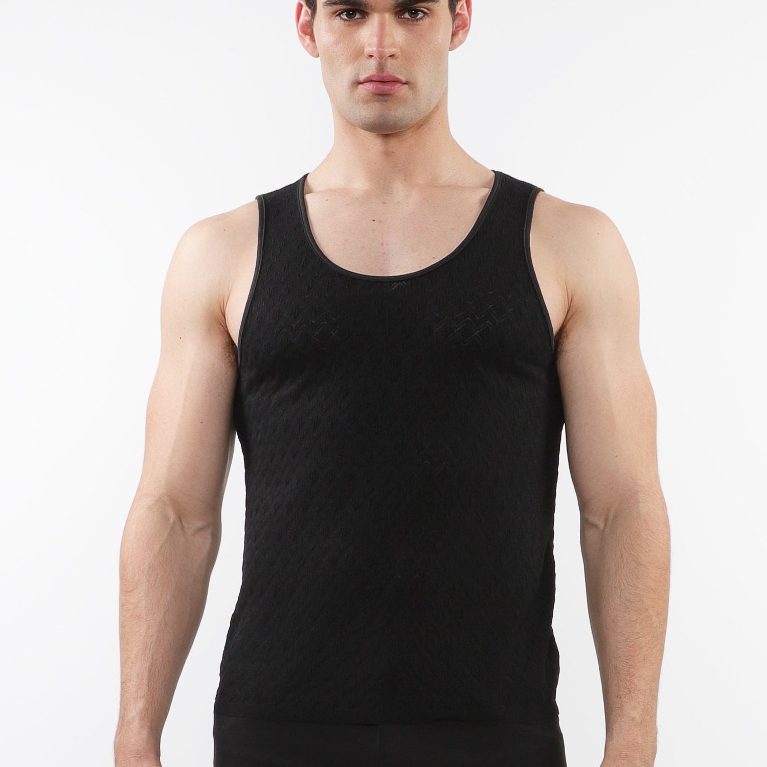 A male model wearing a black stretch knit tank top with a scoop neckline and sleeveless silhouette.