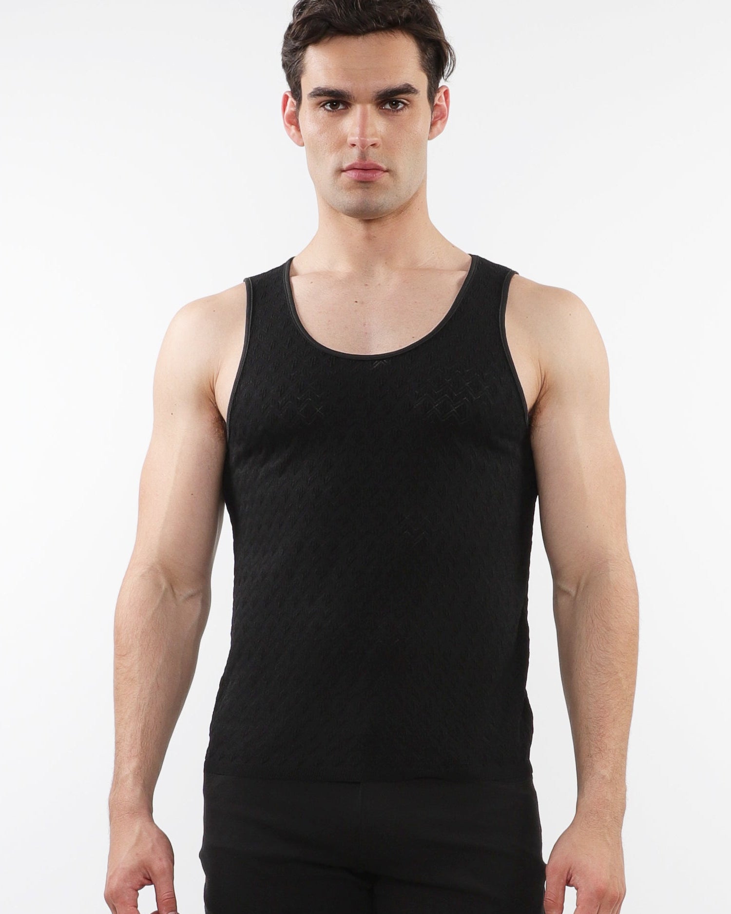 A male model wearing a black stretch knit tank top with a scoop neckline and sleeveless silhouette.