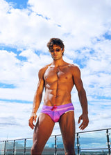 Man in pink swimsuit standing on a rooftop with a blue sky and clouds in the background