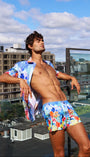 Man in colorful swim trunks standing on a rooftop with cityscape in the background