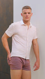 Man wearing a striped shirt and shorts standing against a textured wall.