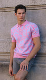 Man wearing a pink polo shirt leaning against a stone wall.