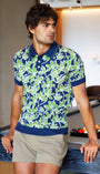 Man in a patterned shirt standing next to a pool table in a modern room.