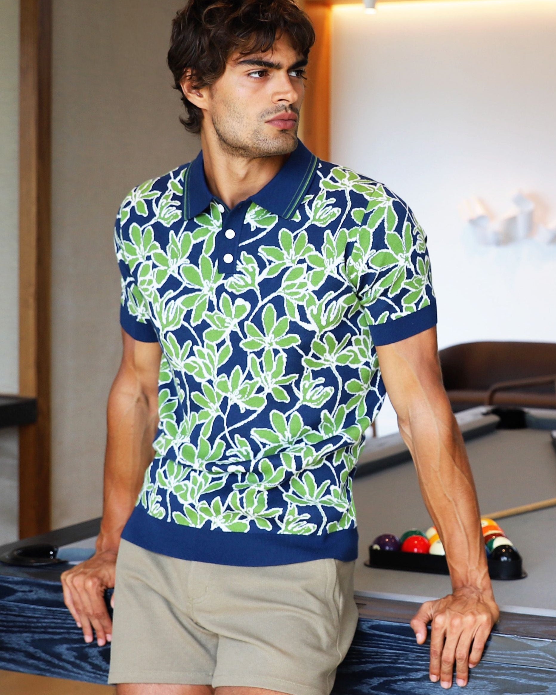 Man in a patterned shirt standing next to a pool table in a modern room.
