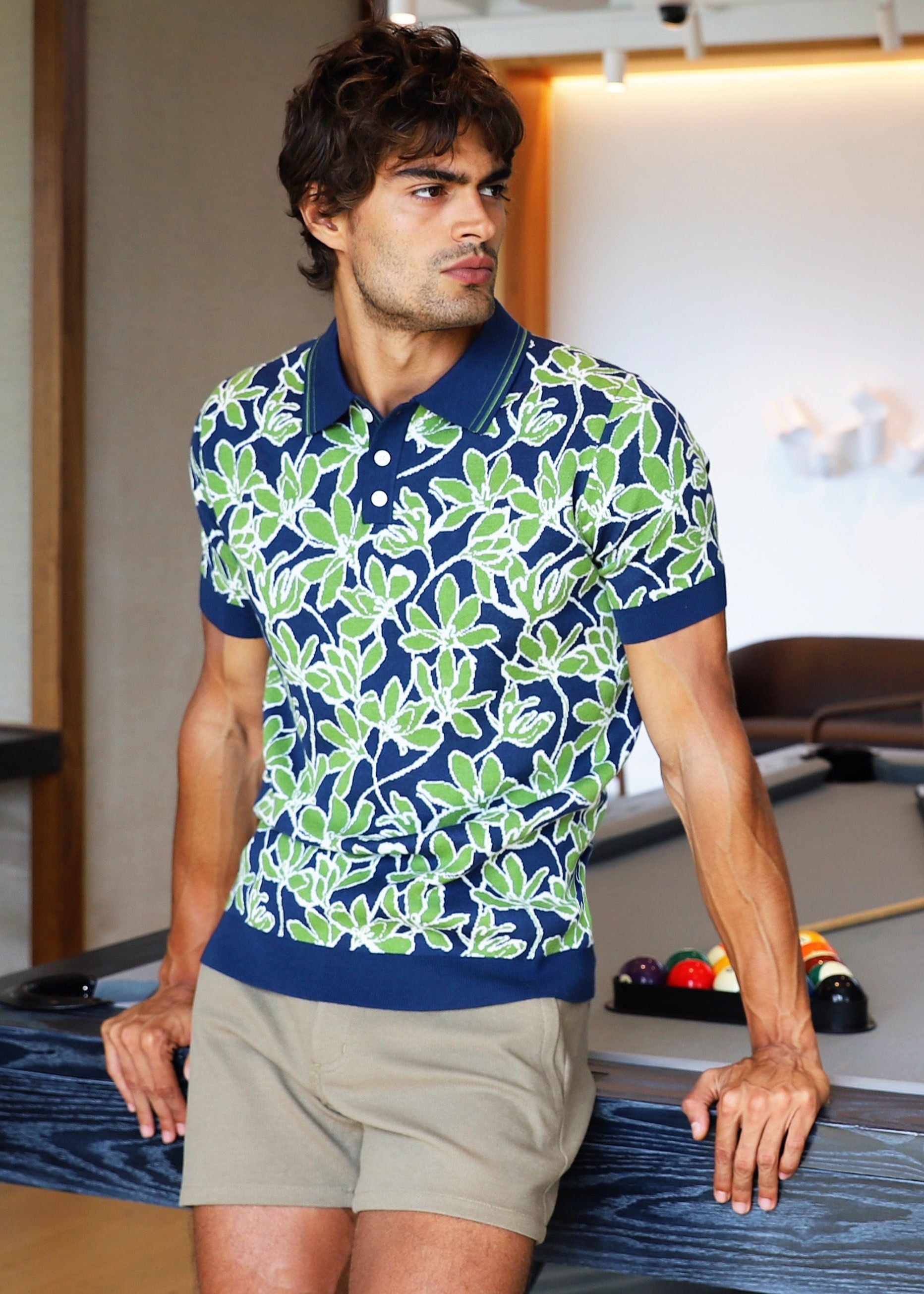Man in a patterned shirt standing next to a pool table in a modern room.